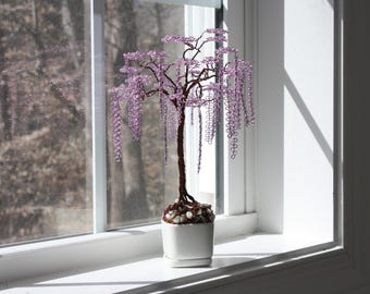 May include: A purple beaded wire tree with a white ceramic pot. The tree is shaped like a weeping willow with long, cascading branches.