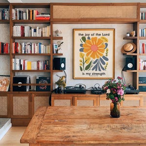 May include: A wooden table with a floral print framed artwork on the wall behind it. The artwork features a yellow flower with blue and green leaves and the text "the joy of the Lord is my strength".