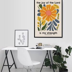 May include: A framed print with a yellow flower and green leaves on a white background. The text "the joy of the Lord is my strength" is written in black text below the flower. The text "Nehemiah 8:10" is written in smaller black text below the main text.