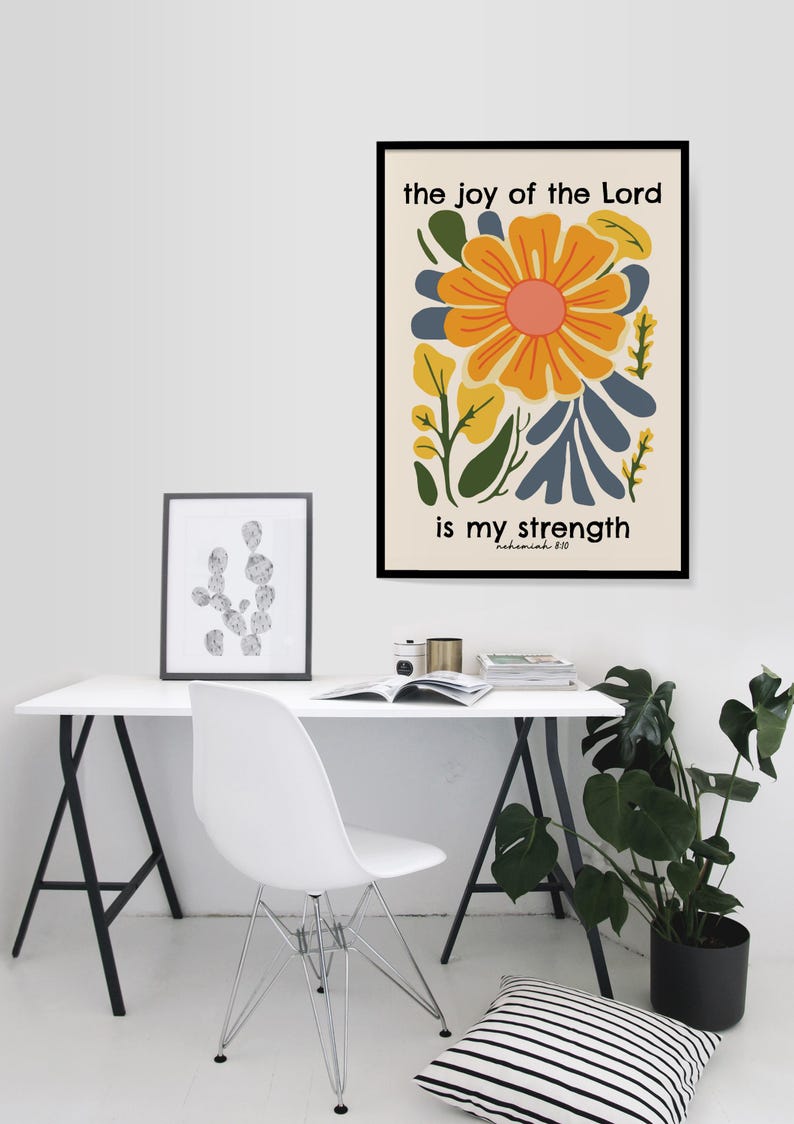 May include: A framed print with a yellow flower and green leaves on a white background. The text "the joy of the Lord is my strength" is written in black text below the flower. The text "Nehemiah 8:10" is written in smaller black text below the main text.