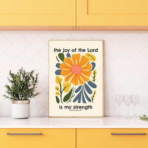 May include: A white poster with a colorful floral design and the text "the joy of the Lord is my strength" in black lettering.
