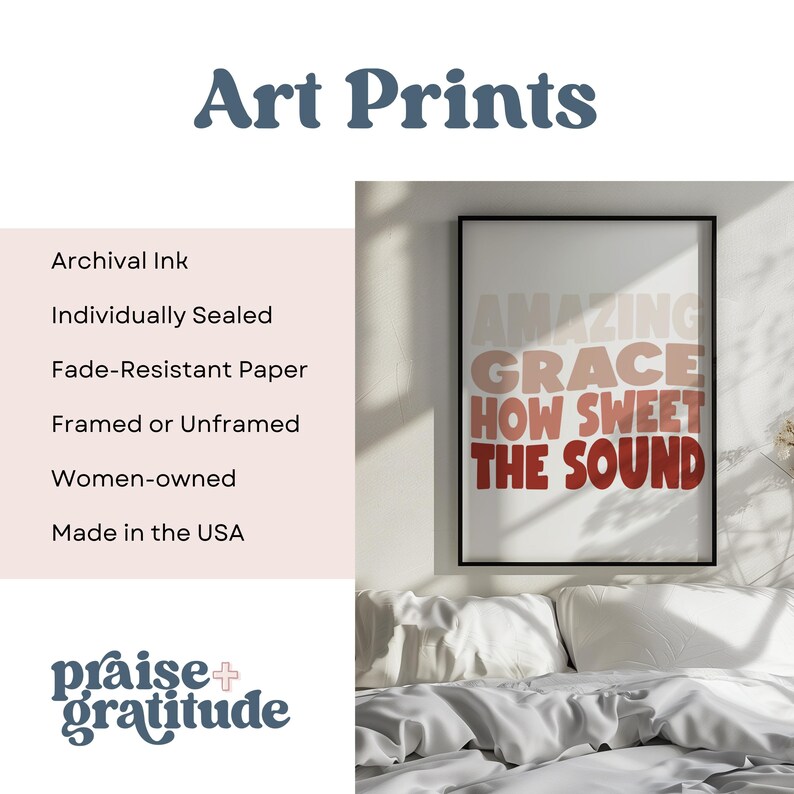 May include: A framed art print with the text "AMAZING GRACE HOW SWEET THE SOUND" in a gradient of pink, orange, and red. The print is on a white background and is framed in a black frame. The print is hanging on a wall above a bed with white bedding.