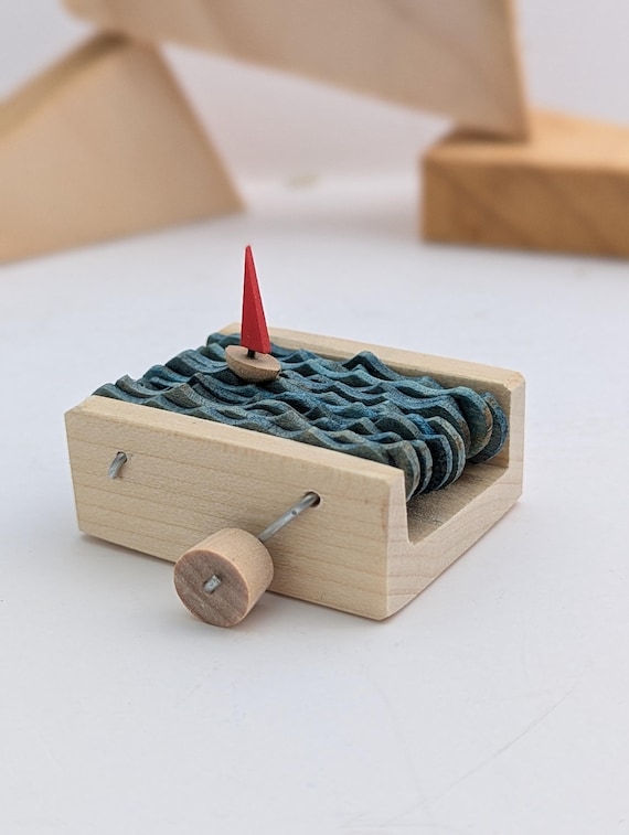 A hand-carved wooden sailboat automaton where the hull rocks and sails move — mechanical maritime magic you wind up and watch sail nowhere, beautifully.