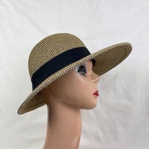 May include: A woven straw hat with a wide brim and a black band. The hat has a neutral color scheme with a black band around the crown. The brim is wide, providing ample shade. The hat is displayed on a mannequin head.