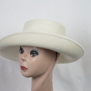May include: A cream-colored hat with a wide brim and a flat crown. The hat is made of a soft, felt-like material and is displayed on a mannequin head. The hat's brim measures approximately 14 inches in diameter.