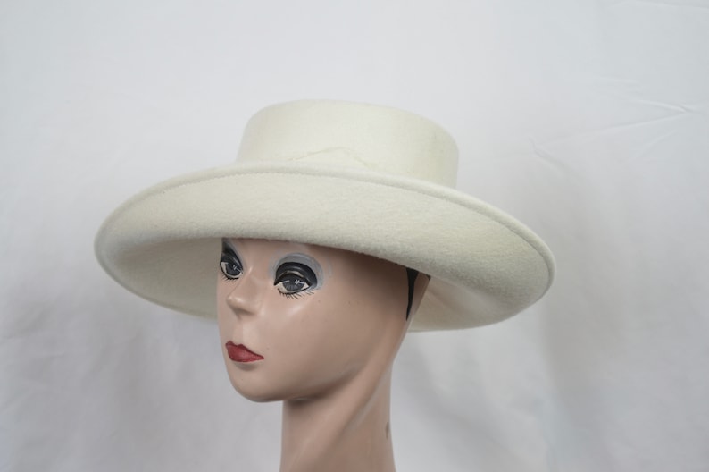 May include: A cream-colored hat with a wide brim and a flat crown. The hat is made of a soft, felt-like material and is displayed on a mannequin head. The hat's brim measures approximately 14 inches in diameter.