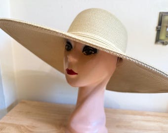 Op de afbeelding: Een hoed met brede rand van stro in een lichtbeige kleur met een afgeronde kroon en een platte, uitgestrekte rand. De hoed heeft een strak geweven textuur, wat zorgt voor een uniform uiterlijk over het gehele oppervlak van het hoofddeksel.