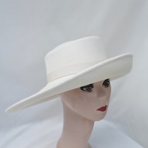 May include: A white fedora-style hat with a wide brim and a matching ribbon band. The hat is displayed on a mannequin head with red lipstick. The hat's brim is approximately 4 inches wide.