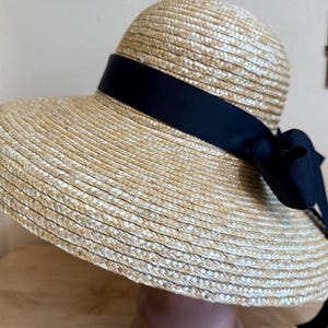 May include: A straw sun hat with a wide brim and a black ribbon tied in a bow. The hat is made of woven straw and has a classic, elegant design. The black ribbon adds a touch of sophistication to the hat.