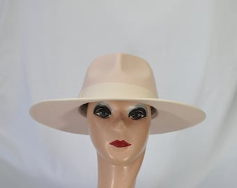 May include: A wide-brimmed hat in a pale pink colour with a white band around the crown. The hat is made of felt and has a smooth finish.