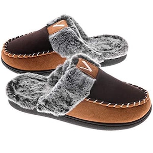 May include: A pair of brown and tan moccasin-style slippers with faux fur trim. The slippers have a dark brown upper, tan suede-like base, and a fluffy gray trim around the opening. White stitching accents the base. A small tan patch with a white V is on the top.