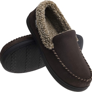 May include: Brown suede-like slippers with a soft, tan faux fur lining and trim. The slippers have a slip-on design with a stitched accent around the opening. The soles are black and textured.