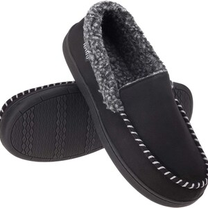 Puede incluir: Zapatillas tipo mocas&iacute;n negras con forro de piel sint&eacute;tica gris y blanco. Las zapatillas tienen una suela negra con un patr&oacute;n texturizado y costuras blancas en los bordes. La marca "VONMAY" es visible en el lateral de una zapatilla.