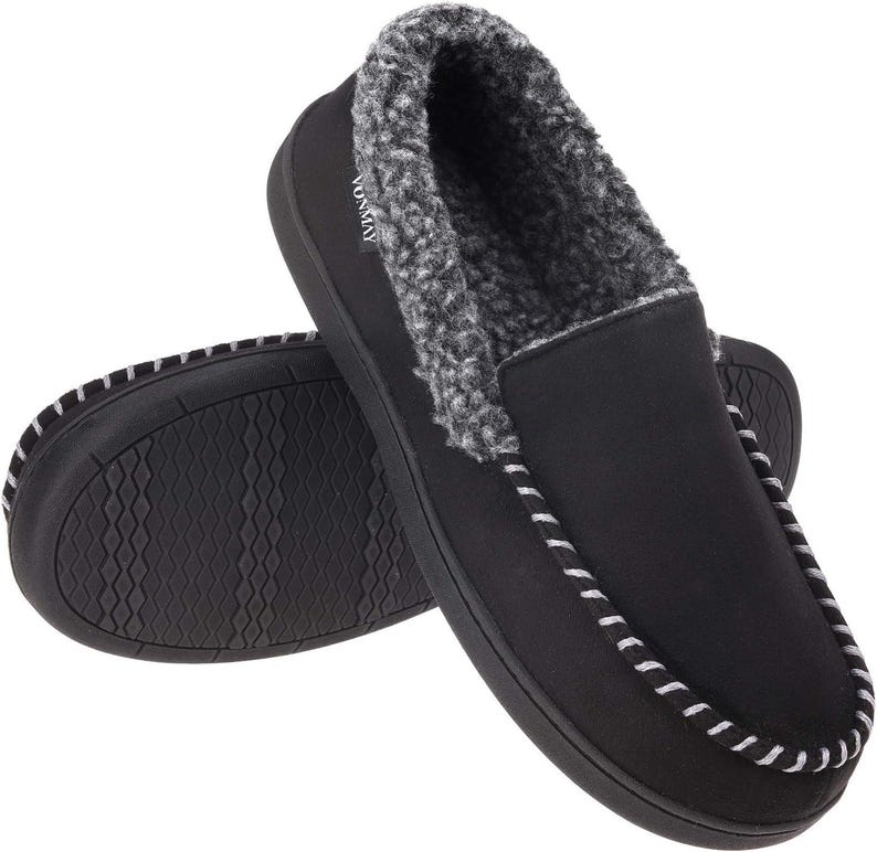 Puede incluir: Zapatillas tipo mocas&iacute;n negras con forro de piel sint&eacute;tica gris y blanco. Las zapatillas tienen una suela negra con un patr&oacute;n texturizado y costuras blancas en los bordes. La marca "VONMAY" es visible en el lateral de una zapatilla.