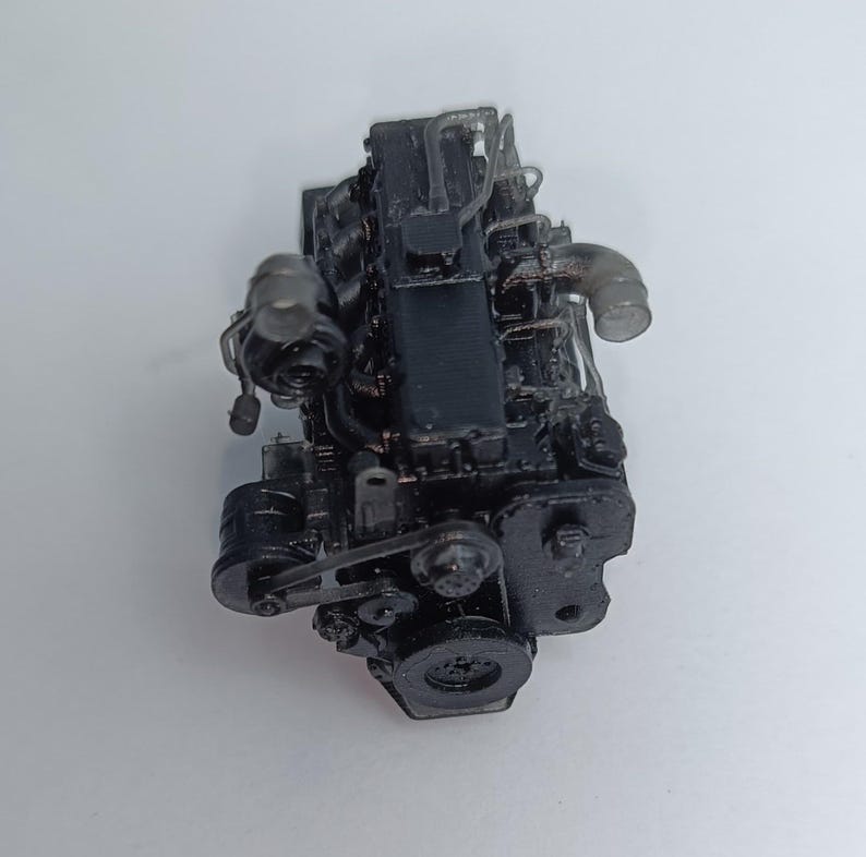 May include: A detailed, black model engine with various components, including pipes, belts, and a flywheel. The engine is set against a plain white background, showcasing its intricate design and mechanical features.