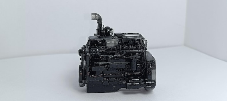 May include: A detailed, black engine model with intricate components, including pipes and various mechanical parts. The engine is set against a plain white background, highlighting its complex design and structure. The model appears to be a miniature replica.