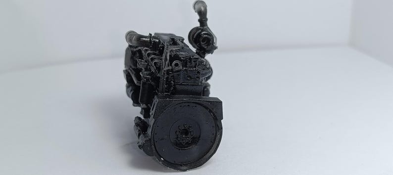 May include: A detailed, black model of an engine, showcasing intricate mechanical components. The model features a cylindrical flywheel and various pipes and tubes, all rendered in a matte black finish. The engine is positioned against a plain white background.