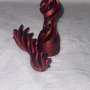 May include: A 3D printed, burgundy-coloured, abstract sculpture with a spiral design. The sculpture is made of multiple pieces that fit together.