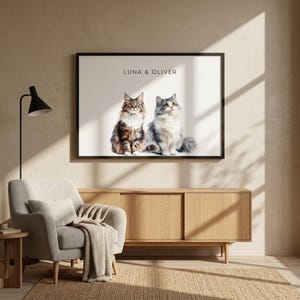 Puede incluir: Impresión enmarcada con dos gatos esponjosos, uno marrón y blanco, el otro gris y blanco, sentados uno al lado del otro. La impresión está etiquetada como "LUNA & OLIVER". La obra de arte se exhibe sobre un mueble de madera.