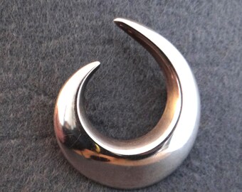 May include: A silver pendant in the shape of a curved, abstract design. The pendant is smooth and shiny.