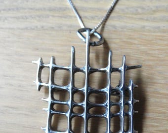 Peut inclure: Un collier avec un pendentif argenté au design géométrique ajouré. Le pendentif présente un motif en forme de grille avec des ouvertures rectangulaires et ovales. La chaîne du collier est argentée. Le pendentif mesure environ 5 cm de large.