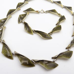 Peut inclure: Ensemble vintage de collier et bracelet. Les bijoux présentent des maillons en forme de feuilles émaillées vert olive avec des accents en métal argenté. Le collier et le bracelet sont présentés sur fond blanc.