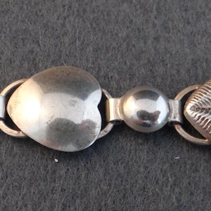 Peut inclure: Bracelet argenté avec un motif répété de maillons en forme de cœur et de feuille. Le bracelet a une finition polie et est relié par de petites perles rondes. Le design est symétrique et les maillons sont reliés par de petits anneaux.