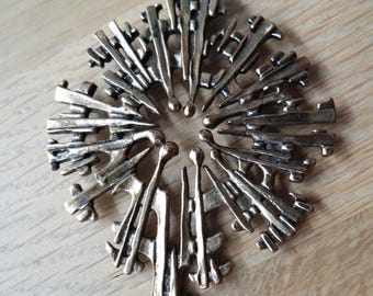 Peut inclure: Un collier pendentif de couleur bronze avec un design géométrique et pointu. Le pendentif est un arrangement circulaire de formes stylisées pointant vers l'extérieur, suspendu à une chaîne sombre. Le collier est présenté sur une surface en bois clair.