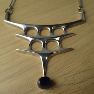 Puede incluir: Un collar de plata con un diseño geométrico y un colgante de piedra azul oscuro.