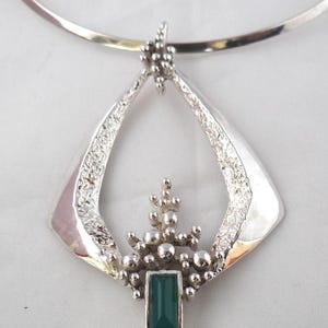 May include: A silver choker necklace with a pendant featuring a textured, open-work design and a green gemstone.
