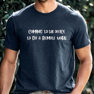 May include: A dark blue t-shirt with white text that reads "Coming to the office to do a remote work."