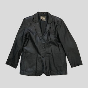 May include: A black leather blazer featuring a notched lapel, two front buttons, and two large patch pockets. The interior neck label displays the text Limited Edition in gold lettering. The jacket has long sleeves and a structured, tailored fit.