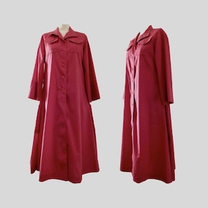 May include: A long-sleeved, floor-length button-down dress in a solid deep red colour. The garment features a pointed collar, two chest pockets with flaps, and a full-length front button closure. The silhouette is loose and flows to the hem.
