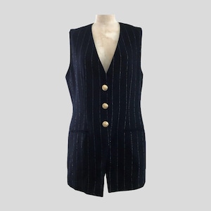 May include: A navy blue pinstripe vest with three gold-colored buttons. The vest has a V-neck and two small pockets. The vest is sleeveless and appears to be made of a woven fabric.