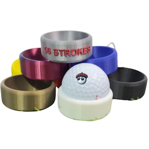Peut inclure: Une pile d'anneaux colorés avec les mots "58 Strokes" imprimés sur l'un des anneaux. Une balle de golf blanche avec un personnage de dessin animé rouge et noir dessus est posée sur les anneaux.