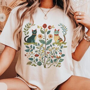 A Cottagecore-inspired shirt featuring whimsical cats and vintage floral patterns, perfect for cat lovers and nature enthusiasts