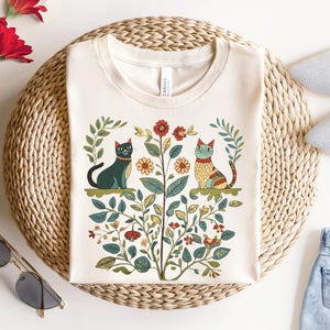 Cottagecore-inspired pink shirt featuring whimsical cats and vintage floral patterns, perfect for cat lovers and nature enthusiasts.