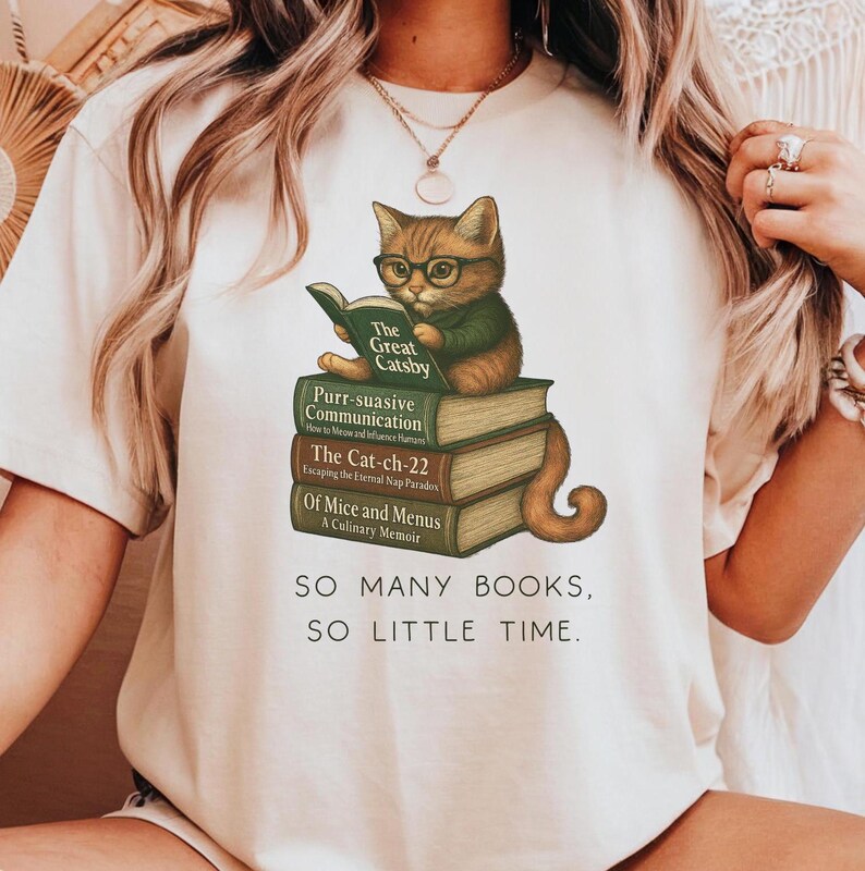 Cute cat lover book-themed shirt featuring an illustrated kitten wearing glasses, reading "The Great Catsby" while sitting on a stack of punny cat books including "Purr-suasive Communication," "The Cat-ch-22," and "Of Mice and Menus." Below the illustration, the text reads: "So many books, so little time."