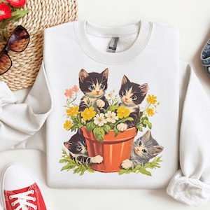 A retro-inspired t-shirt featuring an adorable kitten in a whimsical garden setting with vibrant flowers and vintage-style accents. Perfect for cat lovers and fans of nostalgic, playful designs.