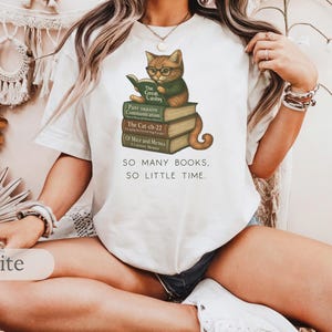 K&ouml;nnte beinhalten: Wei&szlig;es T-Shirt mit einem Grafikdruck eines Katzen mit Brille, das auf einem Stapel B&uuml;cher sitzt. Der Text auf dem Shirt lautet "SO MANY BOOKS, SO LITTLE TIME."