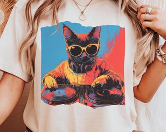 May include: A white t-shirt with a colorful graphic of a cat wearing sunglasses and headphones, mixing music on a DJ turntable.