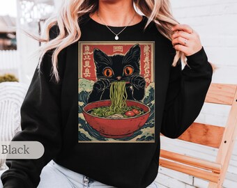 May include: Black sweatshirt with a graphic print of a black cat eating ramen noodles. The graphic is in a Japanese style with a wave pattern in the background. The text on the graphic is in Japanese.