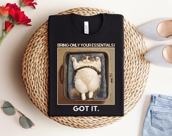 May include: Black t-shirt with a white graphic of a cat in a suitcase. The text "Bring only your essentials! Got it." is printed on the shirt.