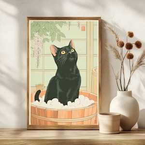 May include: A framed art print featuring a black cat in a wooden tub filled with bubbles. The cat looks upwards with yellow eyes. The background includes a window, green foliage, and a light green wall. The print has a wooden frame.