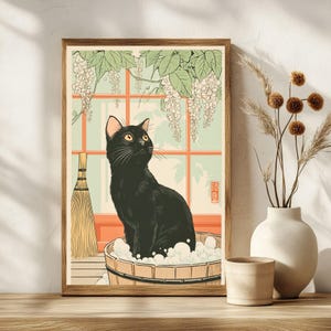 May include: Framed art print featuring a black cat in a wooden tub with bubbles, looking up. The artwork has a Japanese aesthetic, with a window, wisteria, and a broom. The color palette includes black, orange, green, and beige.