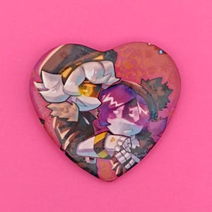 May include: Heart-shaped button featuring two anime-style characters in a close embrace. The characters have white and purple hair, wearing black and yellow outfits. The background is a reddish-brown with small floral accents.