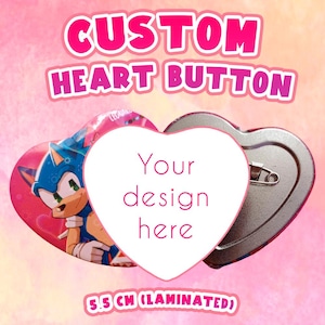 以下が含まれることがあります： ピンバック付きのハート型のカスタムボタン。「CUSTOM HEART BUTTON」のピンク色の文字と中央に「Your design here」の文字が特徴です。ボタンは5.5cm（ラミネート加工）。