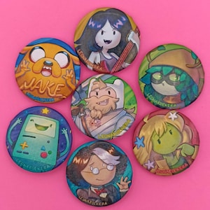 Puede incluir: Una colección de siete botones redondos con ilustraciones coloridas de personajes de dibujos animados. Los botones muestran personajes con varios diseños y el texto "LEONARDOCKERA" está impreso en cada botón. El fondo es de color rosa sólido.