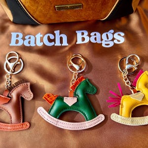 May include: Three rocking horse keychains with different colored leather. The horses are brown, green, and yellow. Each keychain has a silver key ring.