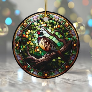 Puede incluir: Un adorno navideño redondo con un diseño de vitral de un faisán posado en una rama con hojas verdes y bayas rojas.